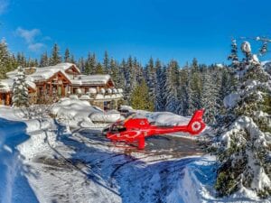 red helicopter in front of snowy ski chalet and trees