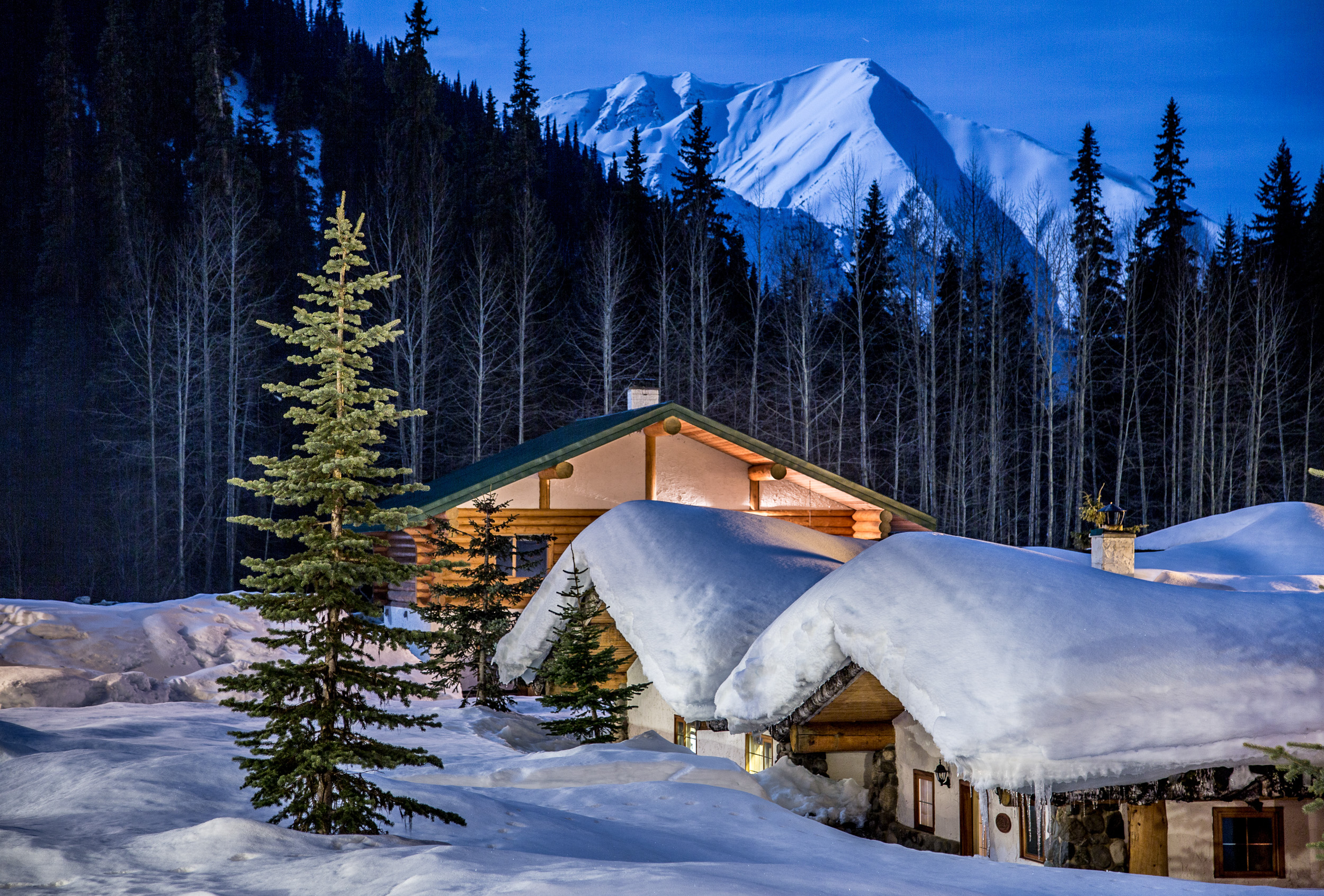 snow covered log cabins with mountains in background