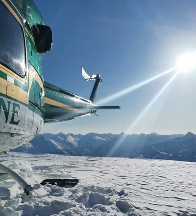 green helicopter in half the picture with the sun in the background surrounded by snow